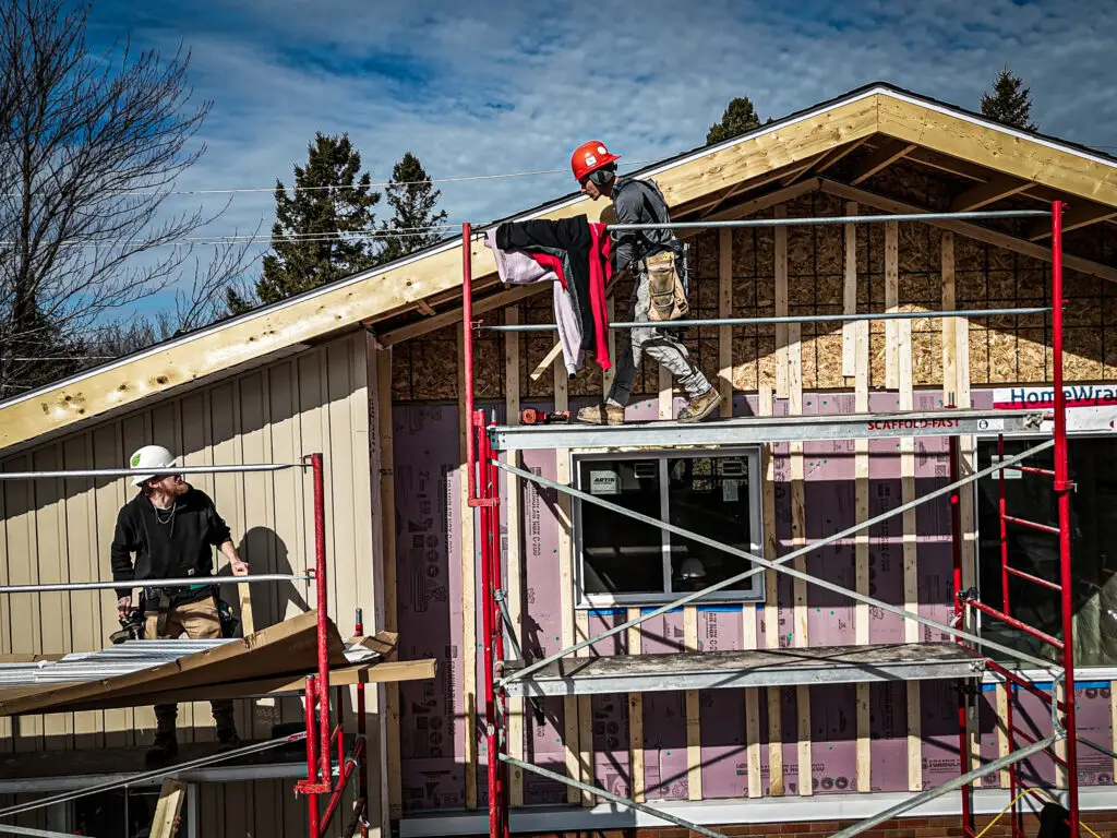 Construction workers on scaffolding installing siding and insulation on a house addition.