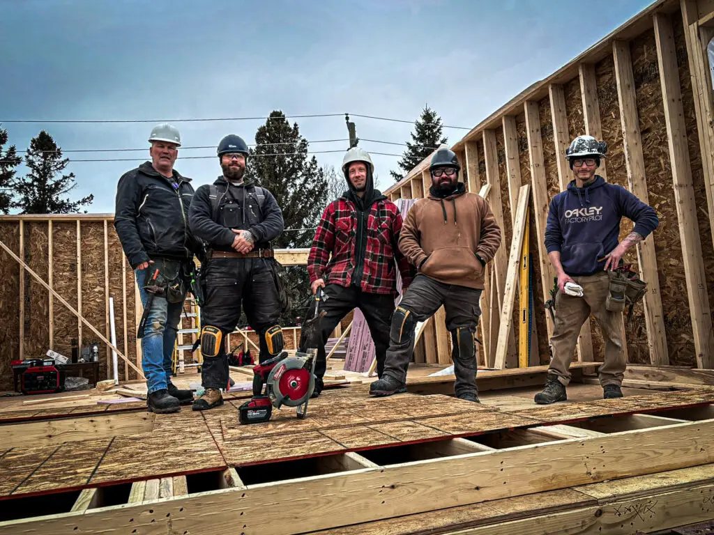 Group of Reno Ottawa workers standing on a wooden framework of a house under construction, showcasing teamwork and construction progress.