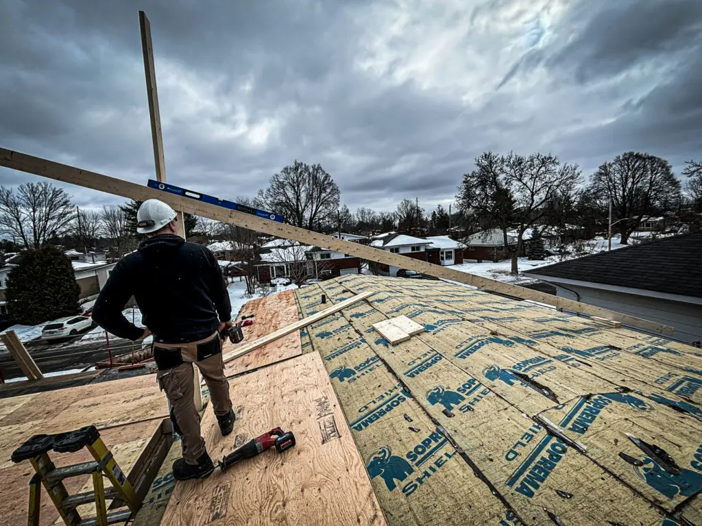 Construction worker standing on a roof covered in insulation and plywood under a cloudy sky. Checking the pitch or level of the roof before setting trusses.