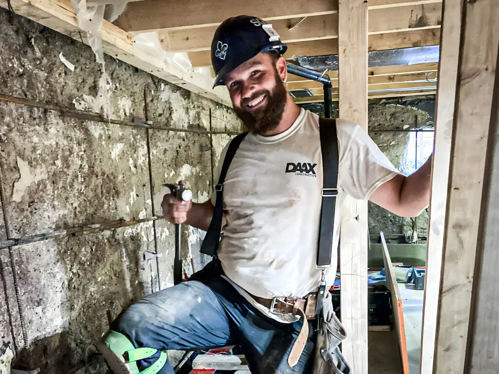 Construction worker smiling while working on framing for a foundation renovation project.